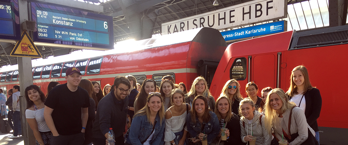 A group of students pose in front of a train at the Karlsruhe Hauptbanhof