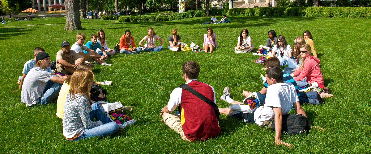Students gather in a seated circle on the grass during orientation. 