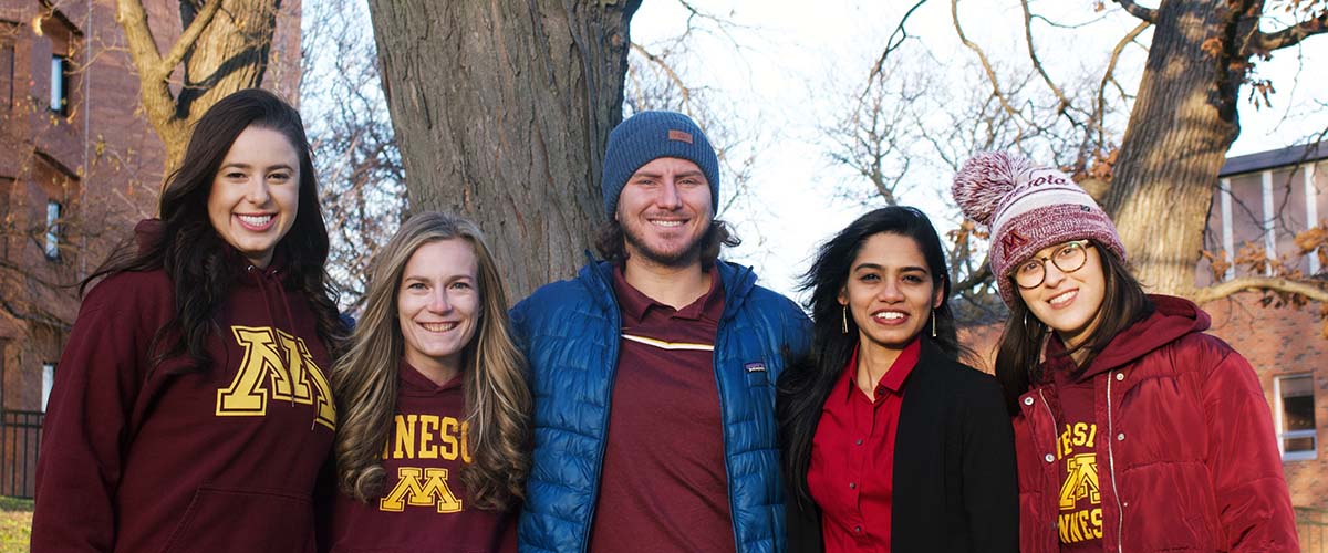 Five students pose together in front of a tree.