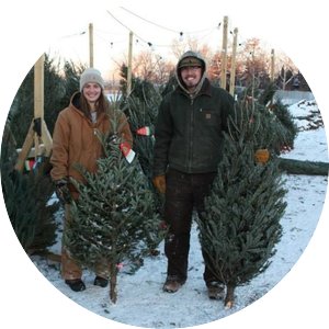Two students hold up Christmas trees at a tree lot