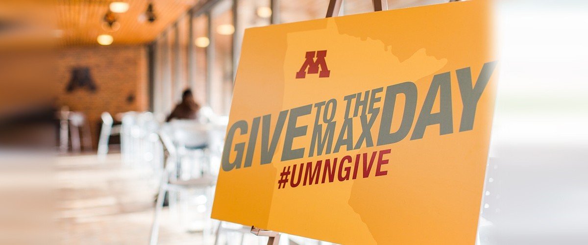 A yellow sign reads " Give to the Max Day #UMNGIVE".