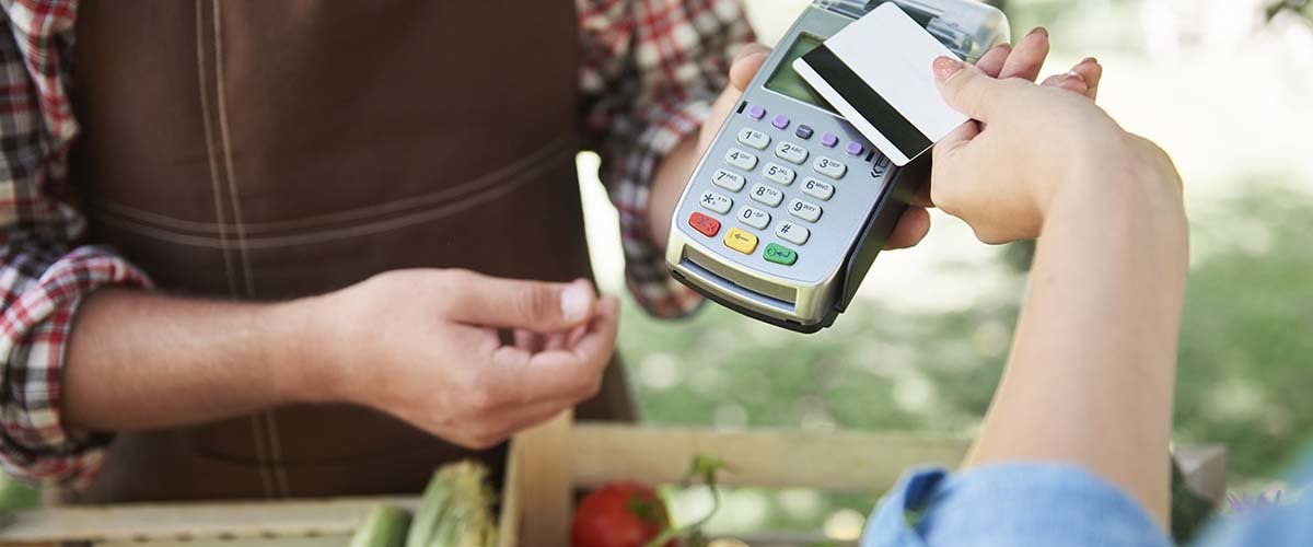 A person paying for produce at a farmer's market with their credit card.