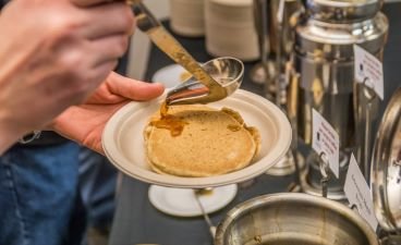 Person ladles maple syrup over pancake