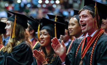 Graduating University of Minnesota students smiling and clapping at a previous year's commencement. 