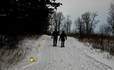 A pair of people walking along a snowy candlelit path