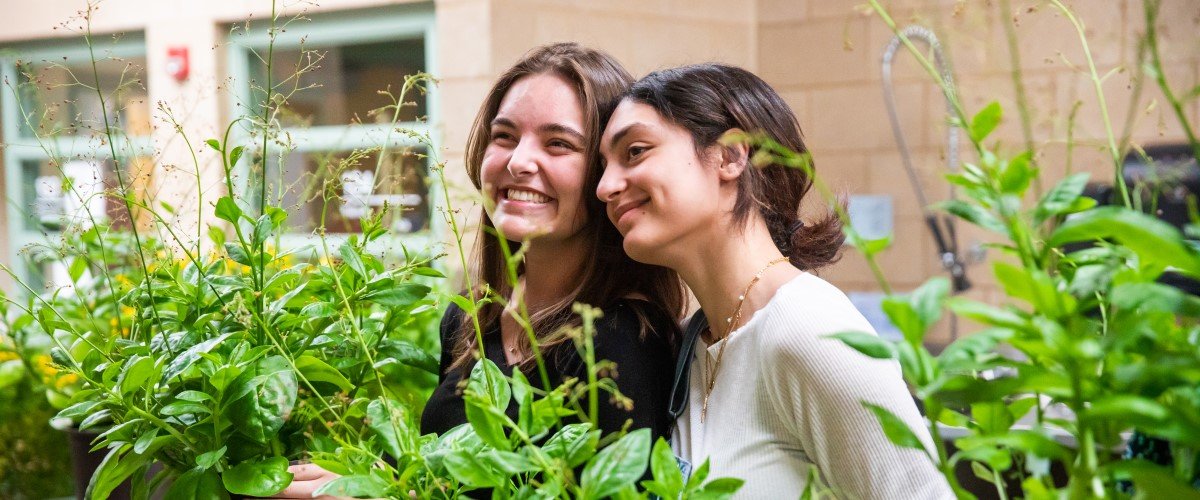 Two students smile holding plants