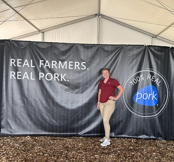 Megan Meyer standing in front of a sign that says Real Farmers, Real Pork. 