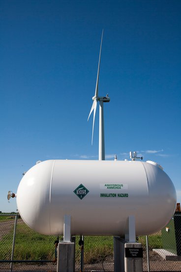A tank of anhydrous ammonia with a wind turbine in the background
