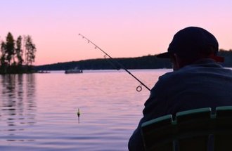 a man sits in a chair and fishes as the sunset makes the lake appear pink.