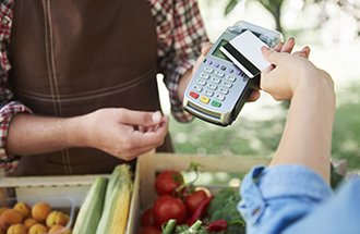 A person paying for produce at a farmer's market with their credit card.