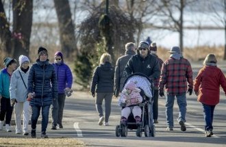 A group of bundled up people walk outside on a trail while trying to maintain social distancing.