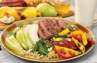 A plate of grilled steak, peppers, and a salad with pears on a table with a glass of milk.