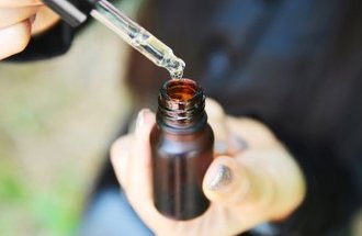 A dropper is held over a brown glass bottle of CBD oil.