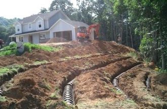 A white house sits on a hill while the septic system gets put in on the hill.