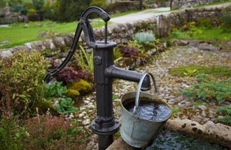 A small fountain and looks like an old fashioned pump spills water into a bucket.