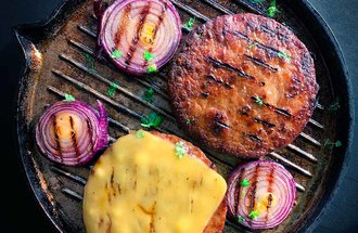 Plant-based burgers on a grill with onions.