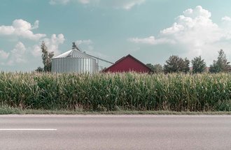 Corn growing in front of a red barn and domed silo.
