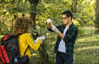 Two students gather research samples in the forest. 