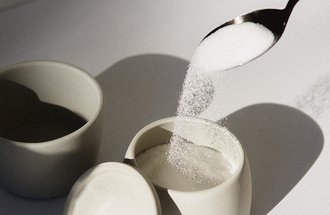 White sugar being poured into a small ceramic dish from a spoon.