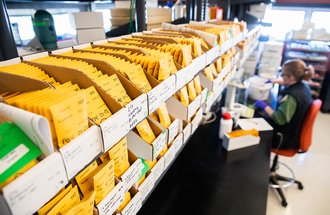 Hundreds of small sample envelopes and a worker running samples in a lab