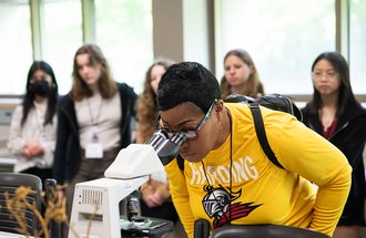 High school student looking into a microscope at MNYI event. 