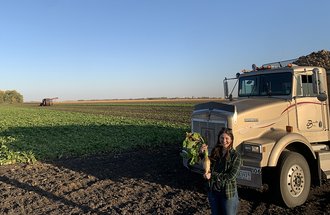 Sam Rude holding a sugar beet in front of a sugar beet field being harvested