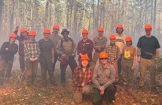 Students wearing orange hard hats standing together in a smoky forest